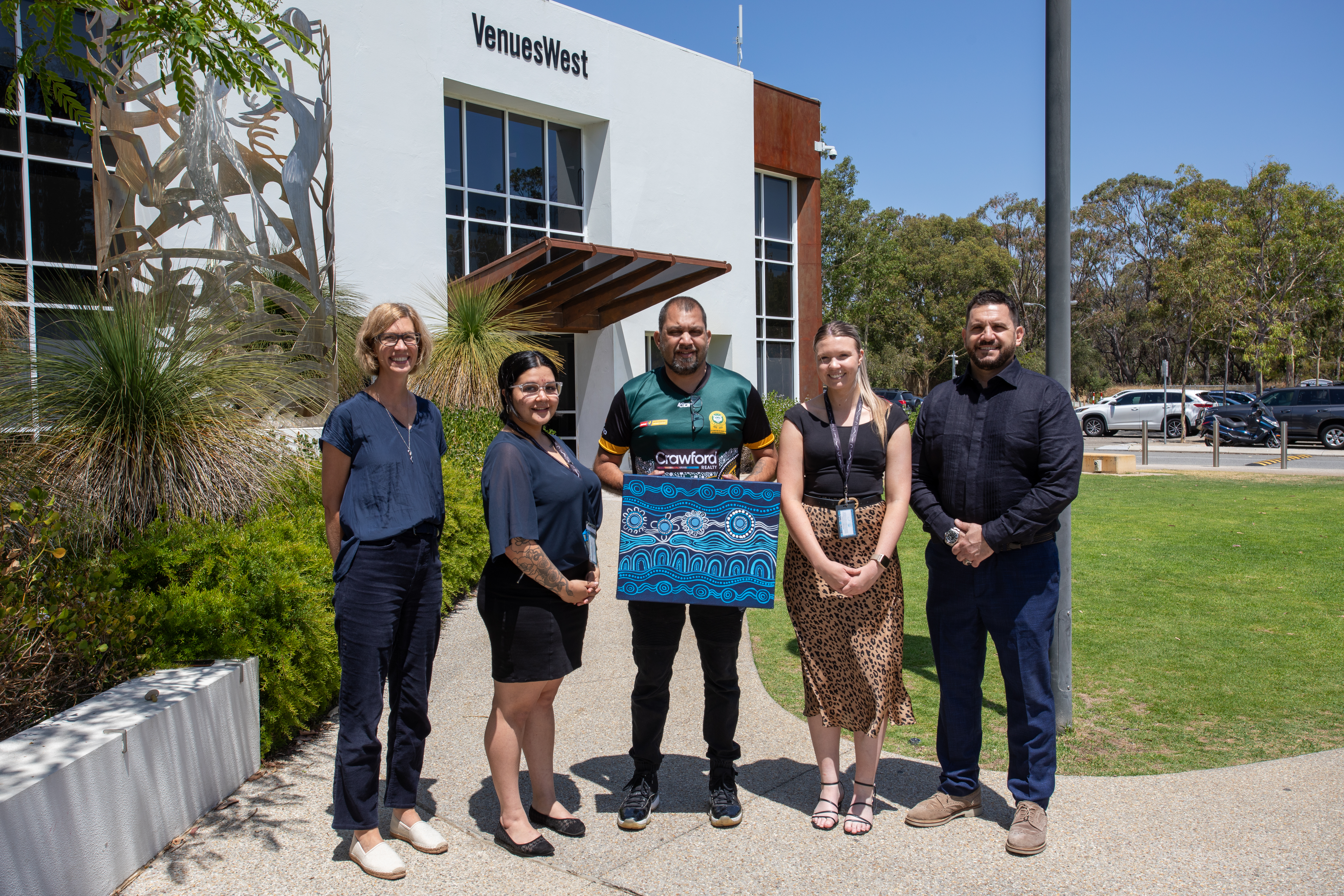 A photo of five VenuesWest employees posing with Indigenous artwork