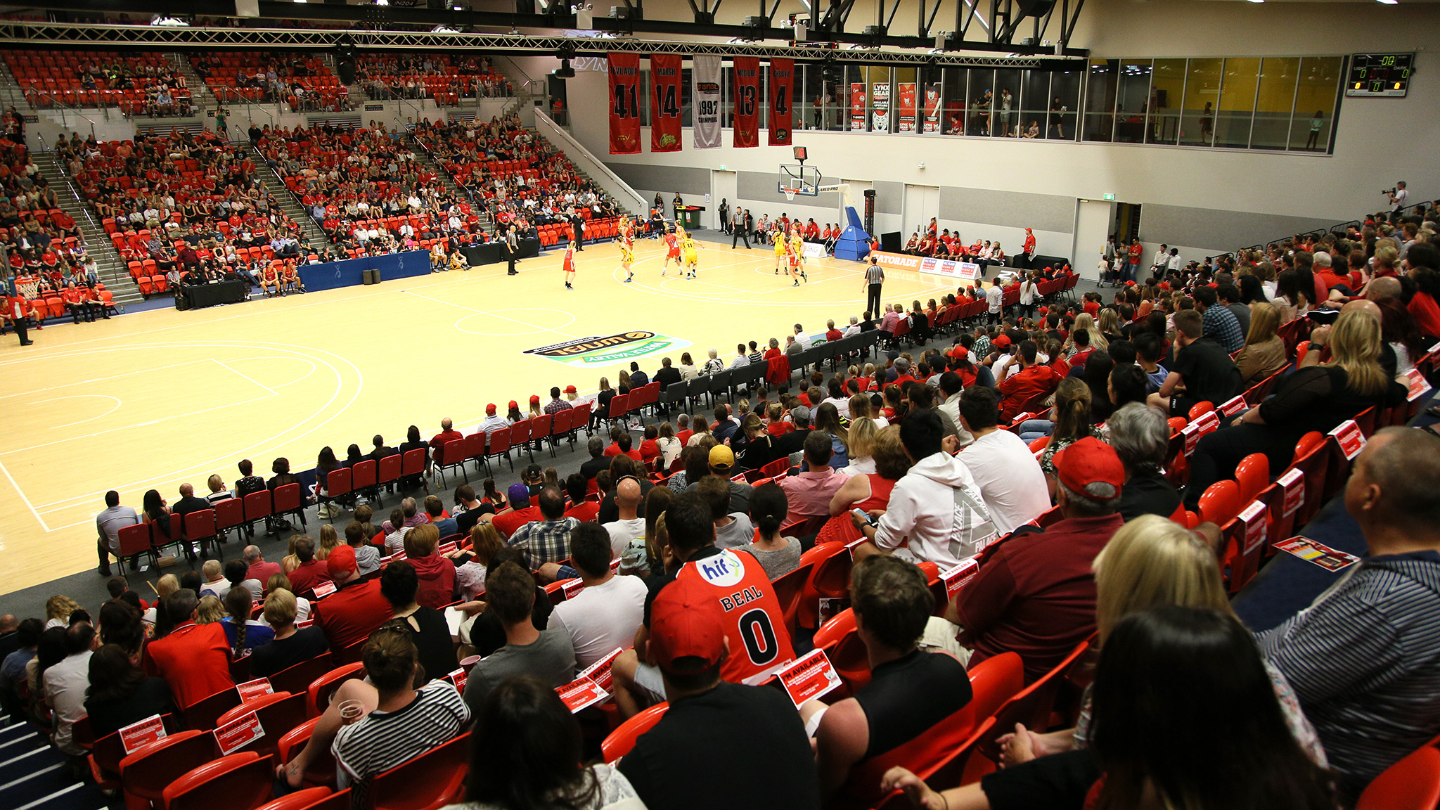 A photo of a packed crowd watching an NBL basketball game being played at the Bendat Basketball Centre
