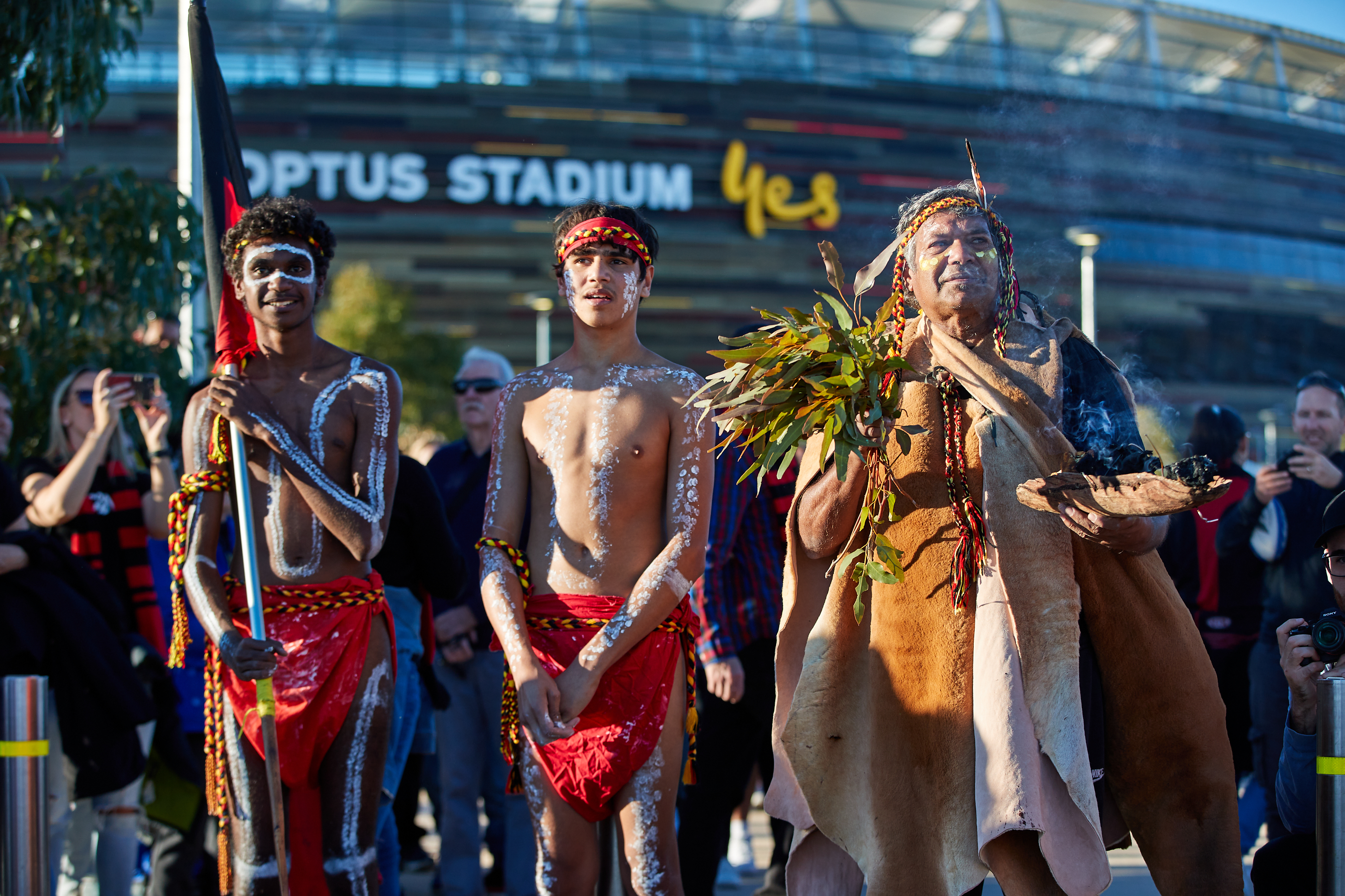 A photo of three Aboriginal elders dressed in traditional clothing outside of Optus Stadium