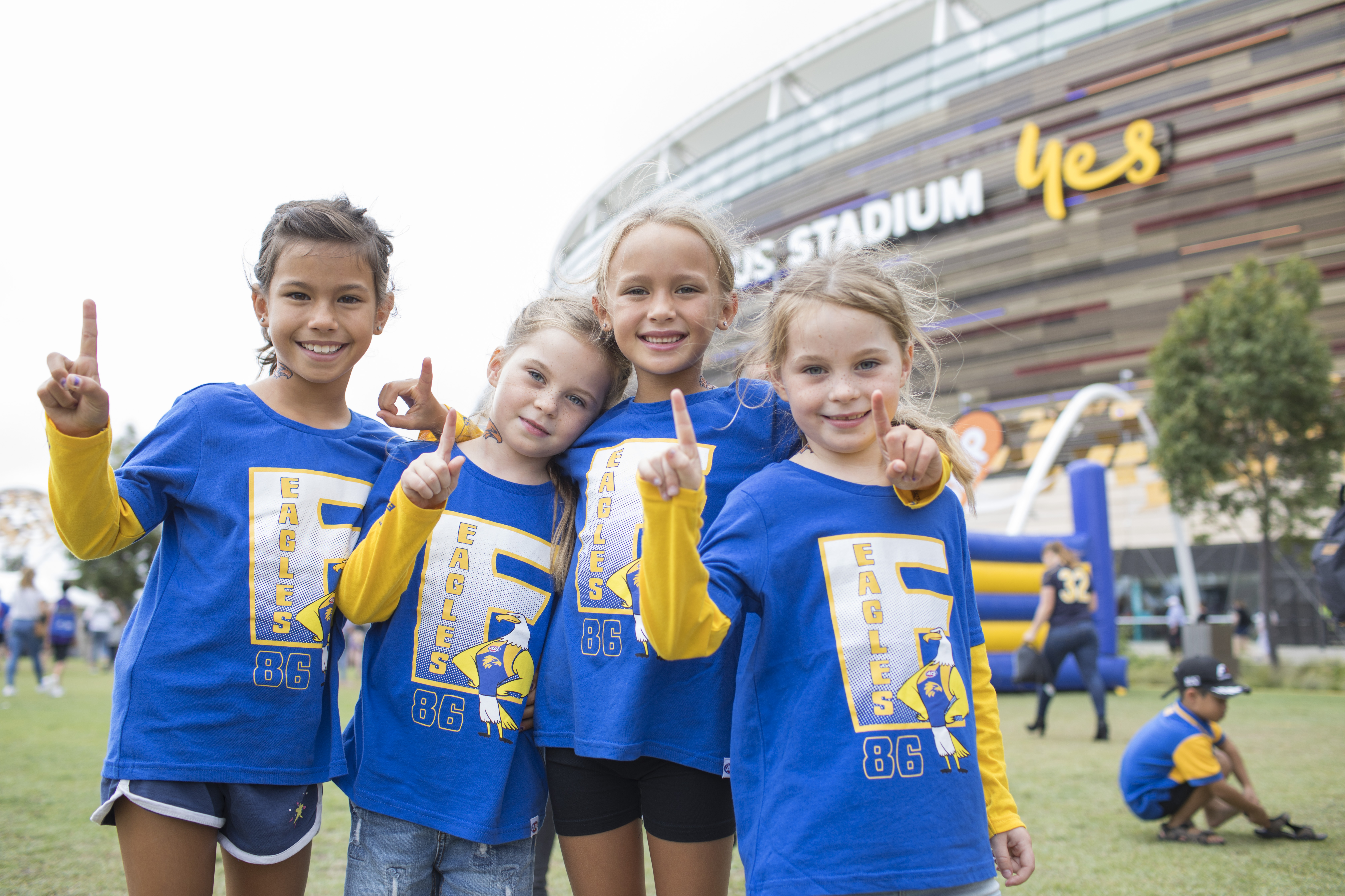 A photo of four children, dressed in West Coast Eagles merchandise, posing outside of Optus Stadium