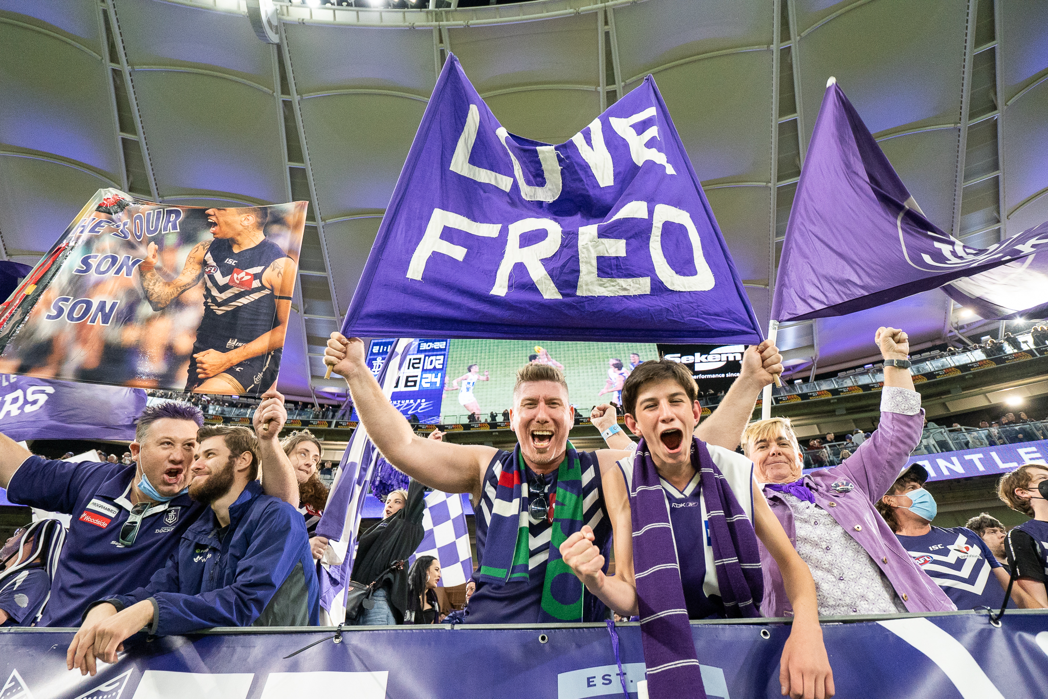 A photo of Fremantle Dockers fans waving flags and celebrating during a game at Optus Stadium