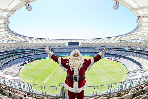 Photo of a person in a Santa suit in the Optus Stadium stands with the field behind them in Burswood, Perth