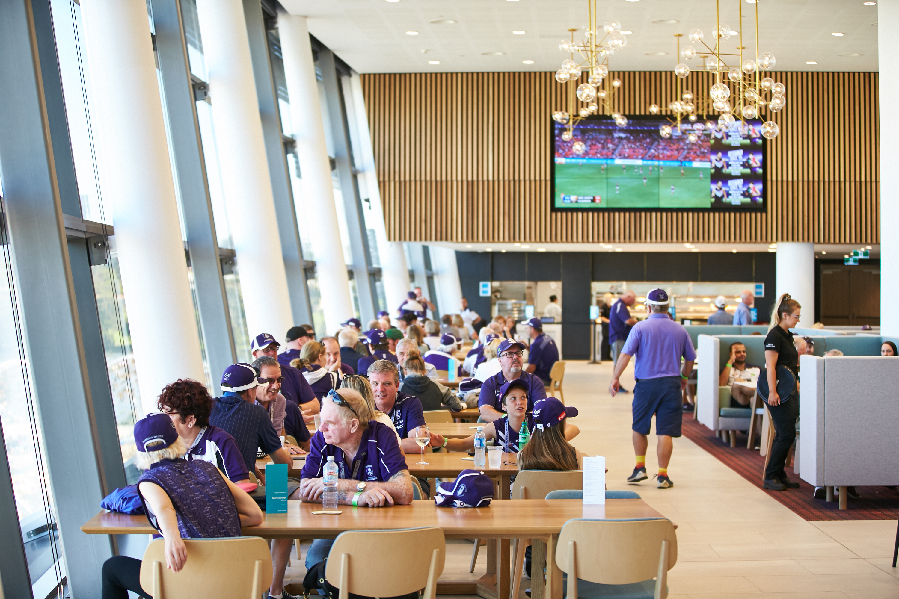 A photo of several tables and chairs full of patrons overlooking the interior of Optus Stadium