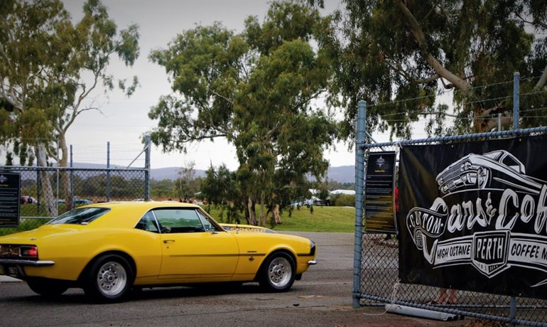 A photo of a car next to a sign advertising the custom cars and coffee event held at the Speeddome in Middle Swan, Perth