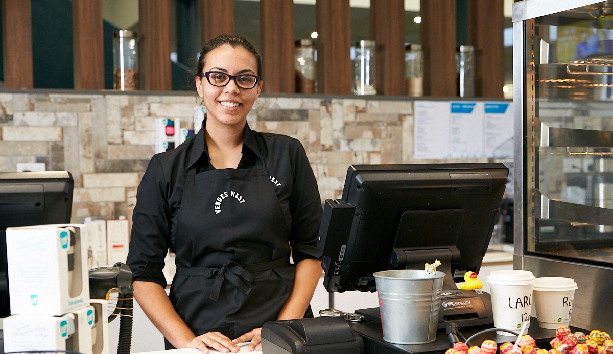 A photo of a woman standing at the counter of a cafe